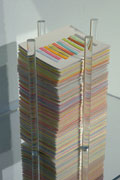 a shelf displaying a stack of cards bounded by clear plexi tubes. each card has a row of paper strips. Strips are embedded with seeds.