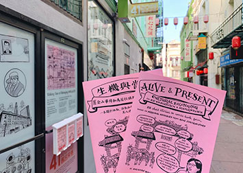 photo of two comic books, one in english, one in chinese, about art, culture and belonging in Chinatown, held up in an alleyway with festive lanterns