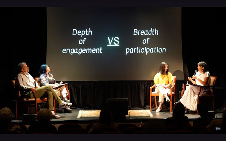 still of video with four panelists on a stage in a theater, with the text on a slide, depth of engagement vs breadth of participation