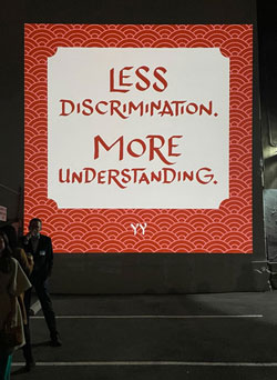 outdoor projection of calligraphy that reads less discrimination, more understanding, yy