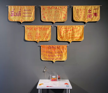 Six banners with marigold backgrounds and calligraphy in red and orange stating: A Space / To be still / To reflect / To release in six languages, above a table with activity cards.