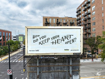 Billboard with the text, How do you keep your heart open, in pencil on paper, in front of red brick apartment buildings