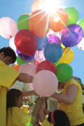 A group of kids and teens circle around an adult to sort out a big bunch of balloons.