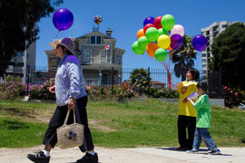 An Asian woman strolls away from adult and child team members handing out ballons along a running path behind the Camon-Stanford house.