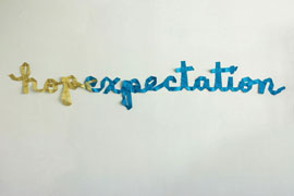 a wall installatin of ribbons spelling the word 'hopexpectation' with hope in gold and expectation in blue.