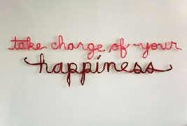 a wall installation of pink and red ribbons spelling out 'take charge of your happiness' in cursive