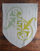 a neutral colored banner whose bottom half is shaped like a shield. it is printed with a floral pattern in light lime green and light green. the pattern is flipped over and positioned so the overall shape is like a letter S.