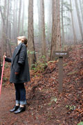 a woman on a trail in the woods. she is looking up. a trail sign nearby states, 'you look up.' 