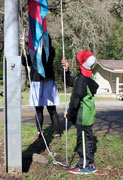 a young boy pulling ropes on a pulley on the base of a large flagpole