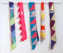 Five colorful sashes hang on a dowel against a white wall.
