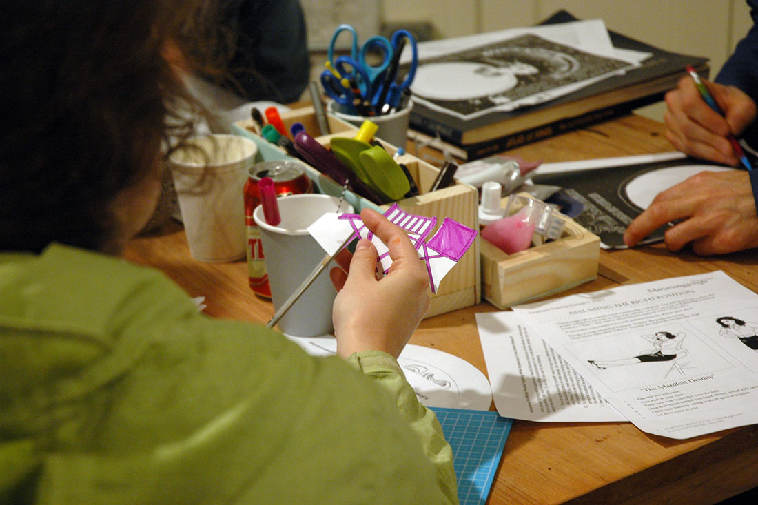 Participants with Pavel Romaniko’s miniature Joseph Kosuth Three Chairs activity (left, in hands), Mail Order Bride’s/M.O.B.’s power positions corporate handbook page (lower right), and Lauren Marie Taylor’s star chart activity (upper right). 