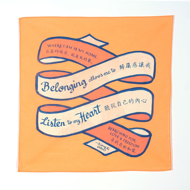 Orange bandanna with a ribbon. On the ribbon says the text in Chinese and English: Where I am is my home. Belonging allows me to listen to my heart, searching for love and freedom. 我在的地方，就是我的家。歸屬感讓我聽從自己的內心尋找自由和愛 Xiang Li (Alice)