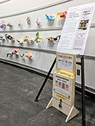 a wood stand with forms and a submission box beneath a sign in front of children's art