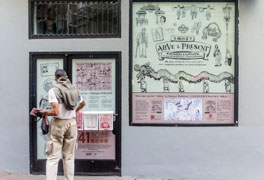 A storefront with the window and door covered in a vinyl that shows drawings from the comic books as well as a monitor and outdoor brochure holders.