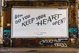 Photo of the artwork as a billboard in a graffitti-covered underpass on a London street.