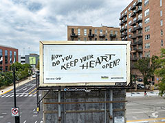 The same artwork on a billboard on a street in Chicago, with a brick apartment building in the background.