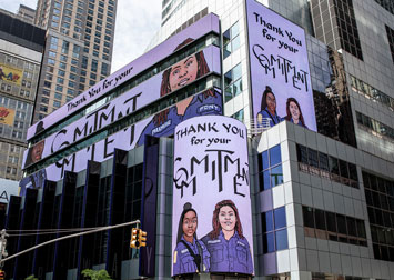 artwork with text Thank You for your Commitment, showing two beautiful black women FDNY paramedics, on billboards on a glass office building in times Square