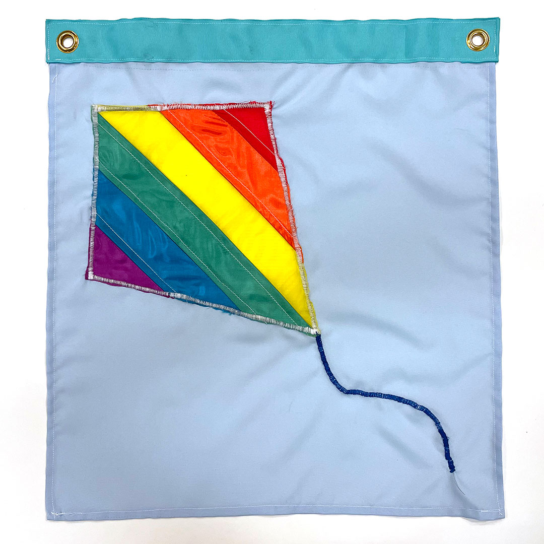 a rainbow pride flag pattern appears on a kite flying on a sky blue background