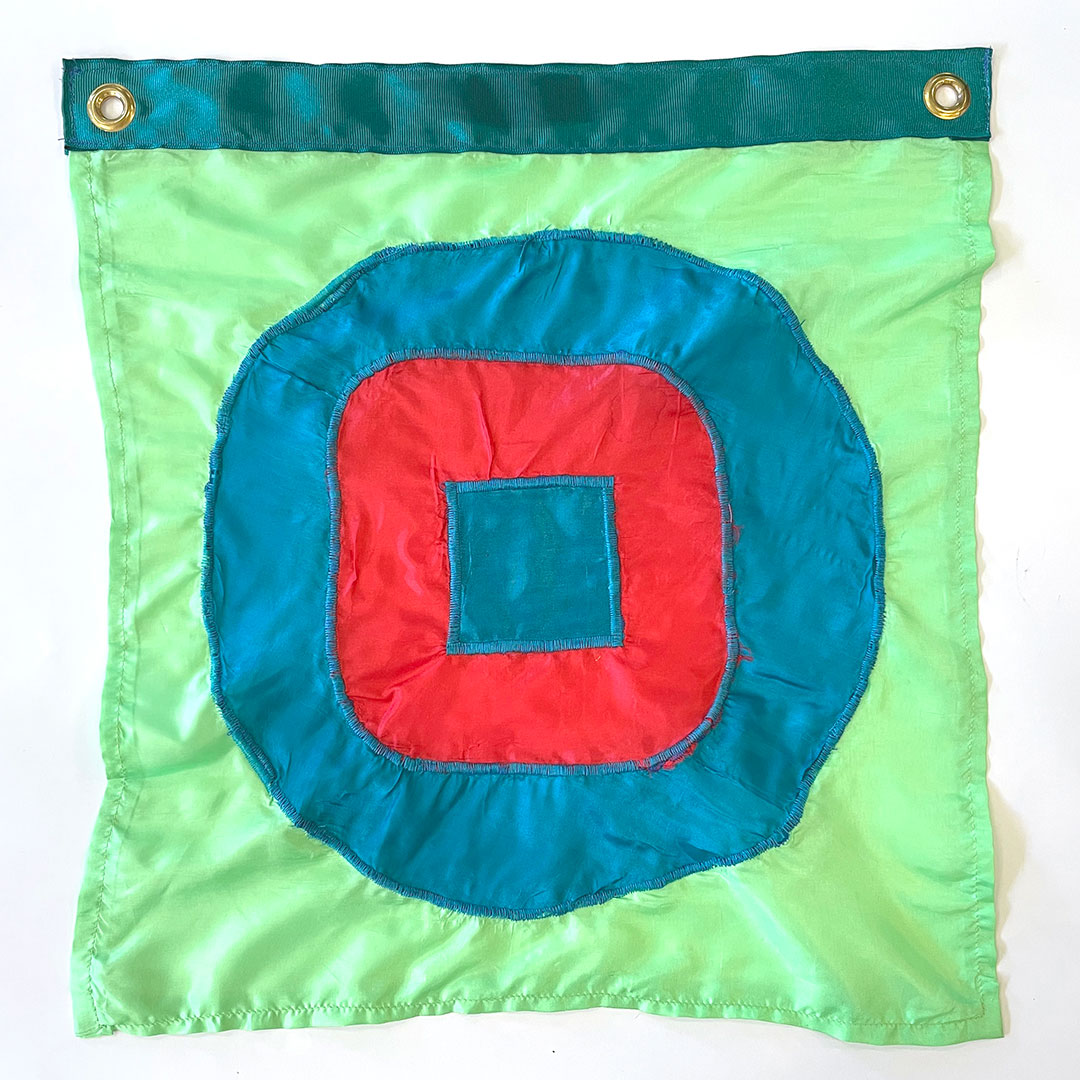 a sewn flag of a blue square inside a red square with rounded corners inside a blue circle on a green background