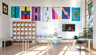photo of several large, colorful flags, hanging on a wall in a room with tables and shelves