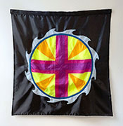 A photo of a flag hanging on a white wall a circle and a cross in yellows, oranges, purples, and blue, with a black background