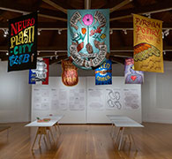 Installation view of the banners in two angled rows forming an octagon beneath open rafters in high-ceilinged gallery.