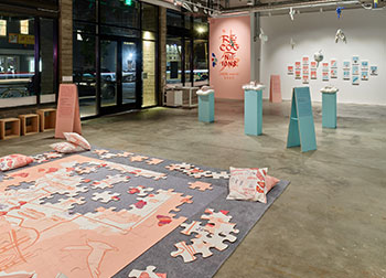Installation view of a gallery with stuffed airplanes, puzzles, and portraits with calligraphy