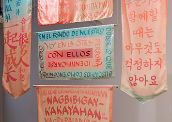 5 banners in pink and blue with calligraphy of various quotes in spanish, tagalog, korean, chinese, and vietnamese