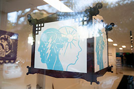 a lantern in a window with a design in blue of two overlapping heads, with a storm from one mind overlapping the sun in another mind