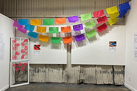 Installation view of project space with papel picado streamers and red Chinese papercuts on windows.